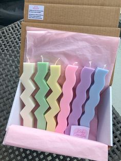 four candles are in a box on a table with some pink and blue wax paper