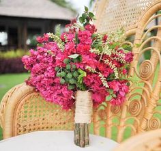 a vase filled with pink flowers sitting on top of a table next to a wicker chair