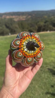 a hand holding a glass bead in the shape of a flower on top of grass