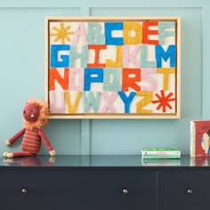 a stuffed animal sitting on top of a dresser next to a framed letter art piece