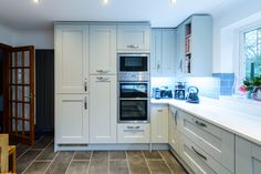 a kitchen with white cabinets and gray tile flooring is pictured in this image, there are two ovens on the counter