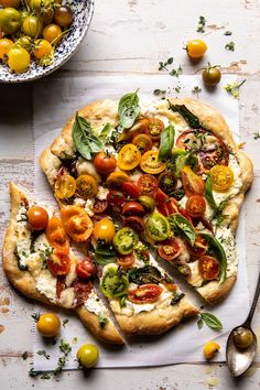 a pizza with tomatoes and basil on it next to a bowl of green olives