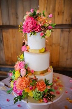 a three tiered wedding cake with flowers on the top and bottom, sitting on a table