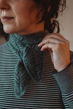 a woman wearing a green and black striped sweater with a scarf around her neck, looking off to the side