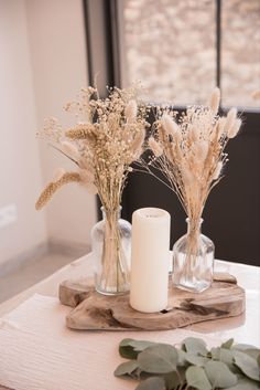 two vases with dried flowers and candles on a wooden tray in front of a window