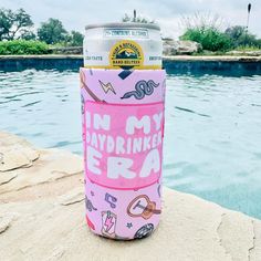 a pink can sitting on top of a rock next to a swimming pool with an in my daydrewn era sticker