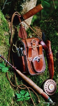 a brown leather bag sitting on top of a moss covered forest floor next to a fishing rod