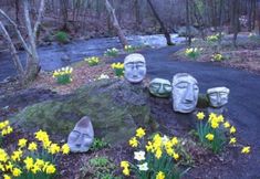 some statues are sitting in the grass near flowers and rocks with yellow daffodils growing out of them