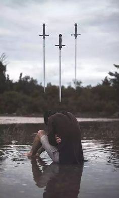 a man kneeling in the water with three swords sticking out of his head above him