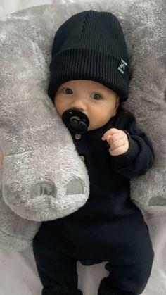 a baby wearing a black hat and holding a stuffed animal