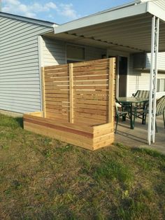 a wooden deck sitting in the middle of a yard next to a white house and green grass