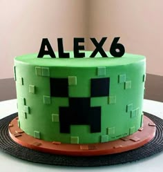 there is a green cake with black letters on it that says alex 6 in front of the cake