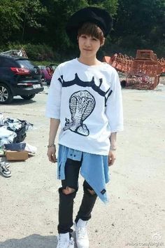 a young man standing in the middle of a parking lot wearing a white shirt and black hat