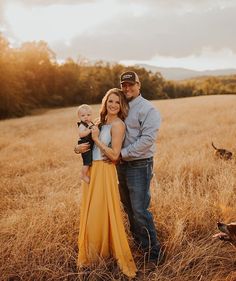 a man, woman and child standing in a field with their arms around each other