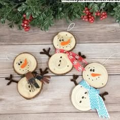 three snowmen made out of wood slices on top of a wooden table next to evergreen branches