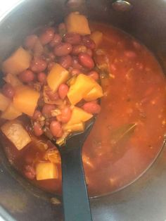 beans and potatoes are being cooked in a pot with a ladle on the side