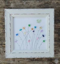 a white frame with colorful flowers and butterflies on it's side, sitting on a wooden