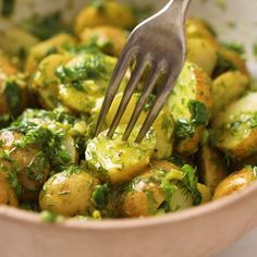 a close up of a fork in a bowl filled with potatoes and broccoli