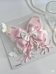 a pink and white butterfly brooch sitting on top of a table next to a glass