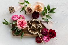 a wooden cutting board topped with flowers and a monogrammed sign that says love