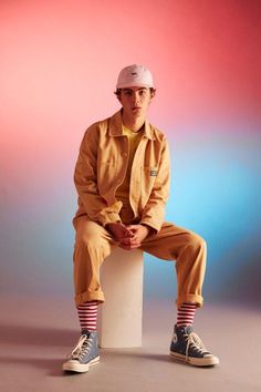 a man sitting on top of a white block wearing a yellow jacket and striped socks