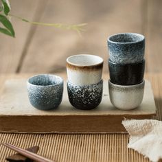 four cups sitting on top of a wooden table next to chopsticks and a plant