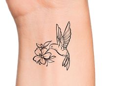 a small hummingbird flying over a flower on the side of a woman's arm