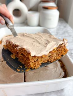 a person holding a spoon over a cake in a pan with frosting on top