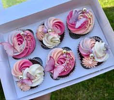 cupcakes with pink and white frosting in a box on the grass outside