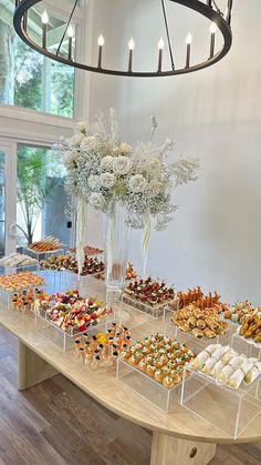 a table filled with lots of desserts on top of wooden tables next to a chandelier