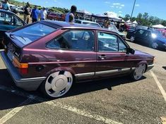 a maroon car parked in a parking lot next to other cars with people standing around