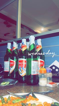 several bottles of beer sitting on top of a counter next to plates with food and utensils