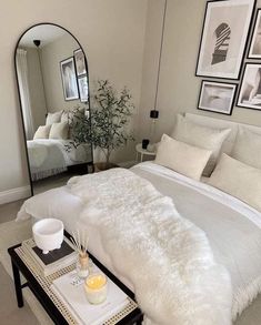 a white bed sitting in a bedroom next to a table with a mirror on it