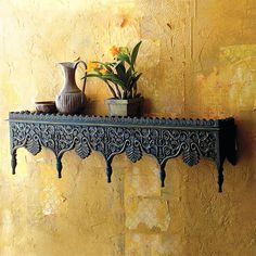 a shelf with vases and flowers on it against a yellow wall in a room