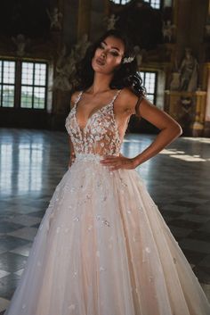 a woman wearing a wedding dress with flowers on the skirt and in front of a large room