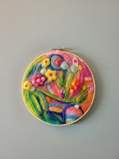 a colorful embroidery on a white wall hanging from a wooden hoop with flowers and leaves