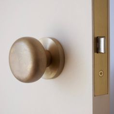 a door handle on the side of a white wall with a gold knob and an open wooden door