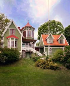 a large green house with red roof and white trim on the top floor, surrounded by greenery