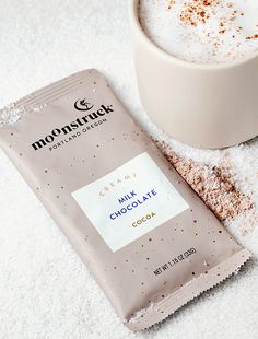 a close up of a bag of chocolate next to a cup on a white surface