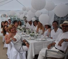 a group of people sitting around a table with plates and cups on it, all dressed in white