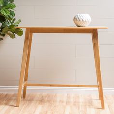 a white vase sitting on top of a wooden table next to a potted plant