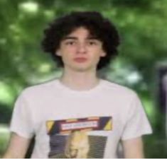 a young man wearing a white t - shirt standing in front of trees