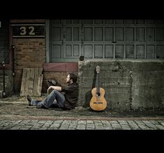 a man sitting on the ground next to a guitar