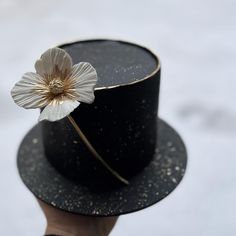 a person wearing a black hat with a white flower on the top and gold rim