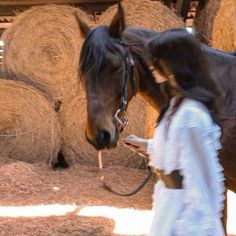 a woman walking next to a horse near hay bales