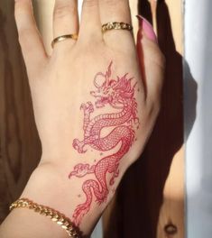 a woman's hand with a red dragon tattoo on her left wrist and gold bracelet