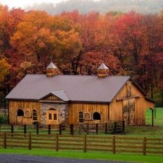 an old barn sits in the middle of a field surrounded by trees with fall colors