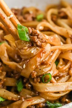 chopsticks holding noodles with meat and vegetables