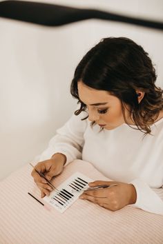 a woman is sitting on her bed and writing in a notepad while holding a pair of scissors