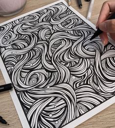 a person is drawing on a piece of paper with black and white ink while holding a pen